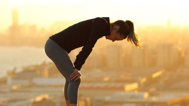 Profile of an exhausted runner resting after running in city outskirts at sunset