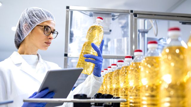 Food inspector or technologist doing quality control of bottled vegetable oil inside bottling plant.