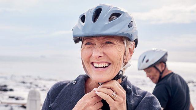 Happy senior woman, bicycle and helmet on holiday ride at beach for fitness workout with man. Smile on face, happiness and health, cycling exercise for mature couple on ocean vacation in Australia.