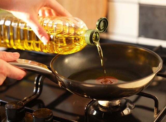 Vegetable fats. Woman pouring oil into frying pan on stove, closeup