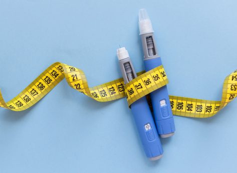 Two injectors dosing pens for subcutaneous injection of antidiabetic medication or anti-obesity medication hovering over a blue background. Yellow measuring tape around the injectors. antidiabetic