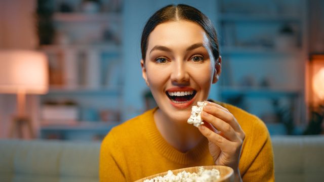 Young woman watching projector, TV, movies with popcorn in the evening. Girl spending time at home.