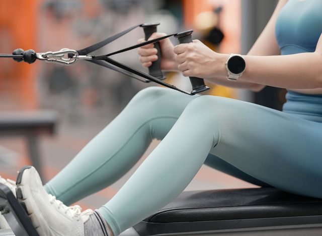 Young woman training on row machine weight training equipment on sport gym.