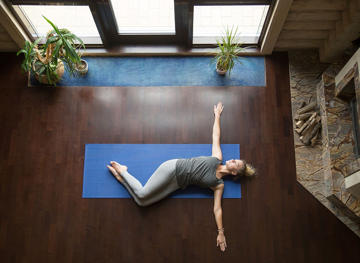 Attractive young woman working out in living room, doing yoga exercise on wooden floor, lying in Belly Twist Pose, Jathara Parivartanasana, resting after practice, full length, top view, Trunk, Rotations, Spinal, Mobility