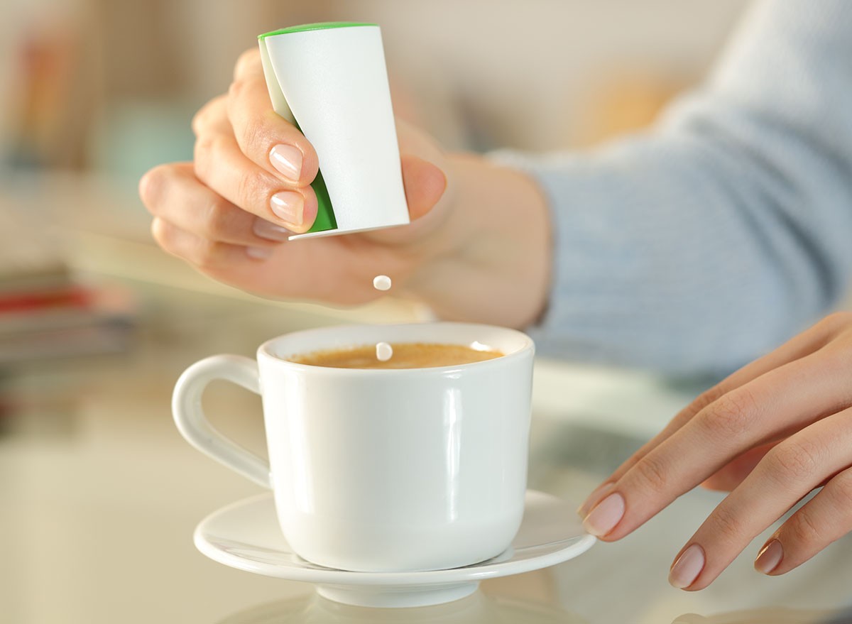 Close up of woman hand throwing saccharin pills on coffee cup on a desk at home
