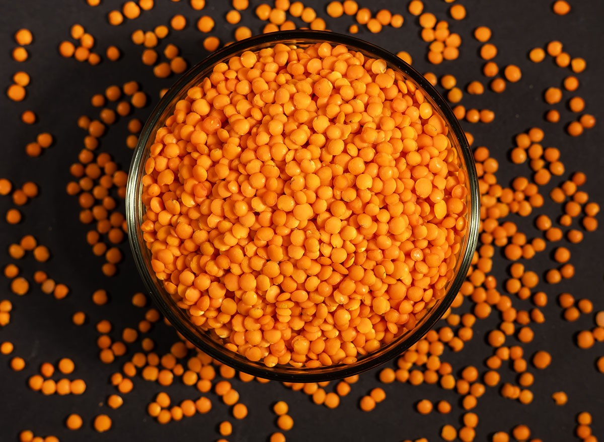 Red lentils in glass bowl. Dry orange lentil grains, heap of dal, raw daal, dhal, masoor, Lens culinaris or Lens esculenta on dark background