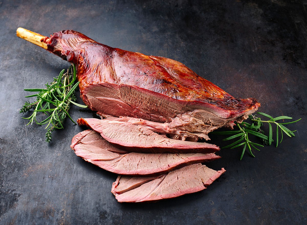 Traditional barbecue leg of venison sliced and served with herbs as close-up on rustic black board with copy space