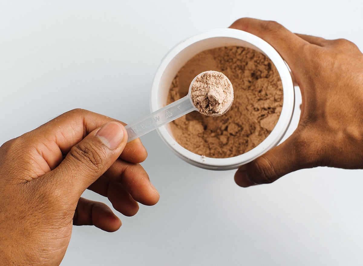 hands holding a scoop of chocolate protein over white background.