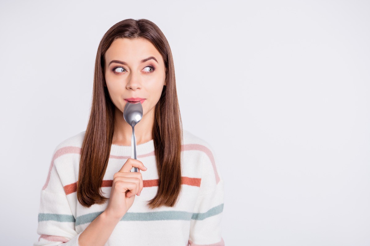 Hungry woman holding spoon in her mouth.