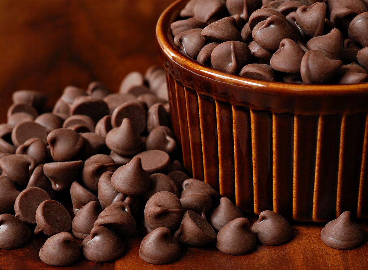 Chocolate chips overflowing from brown ceramic ramekin onto wood table. Macro with shallow dof.