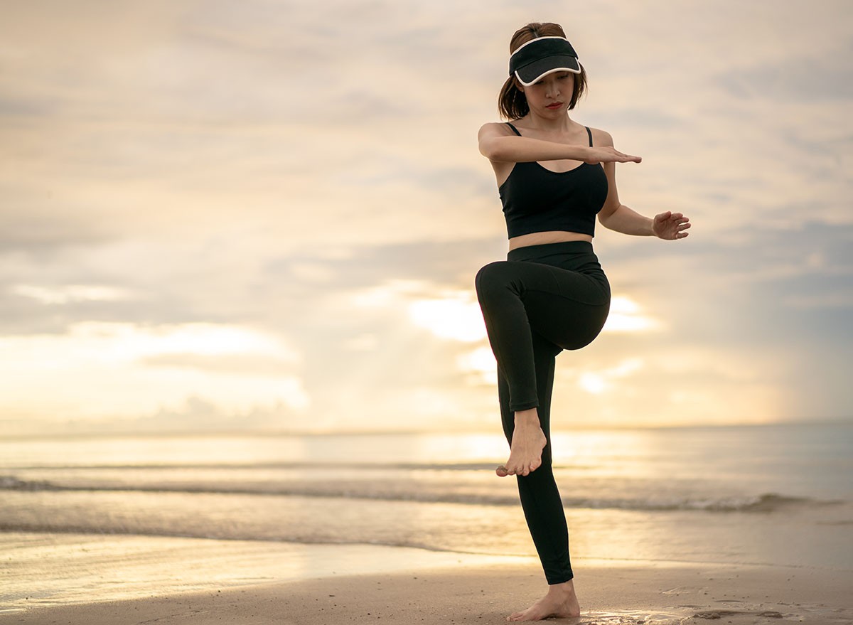 Woman doing high knee twist exercise on the beach with sunrise on the morning. Standing crunches