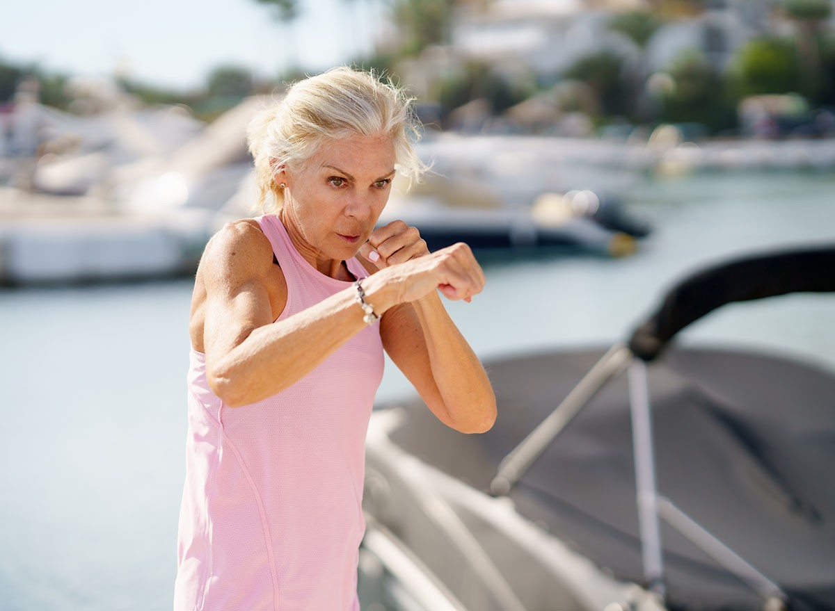 Mature woman doing sport in a coastal port. Arm training throwing boxing punches. Female doing shadow boxing outdoors.