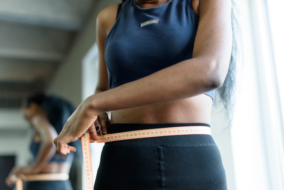 African american woman measuring waist with yellow tape close up.