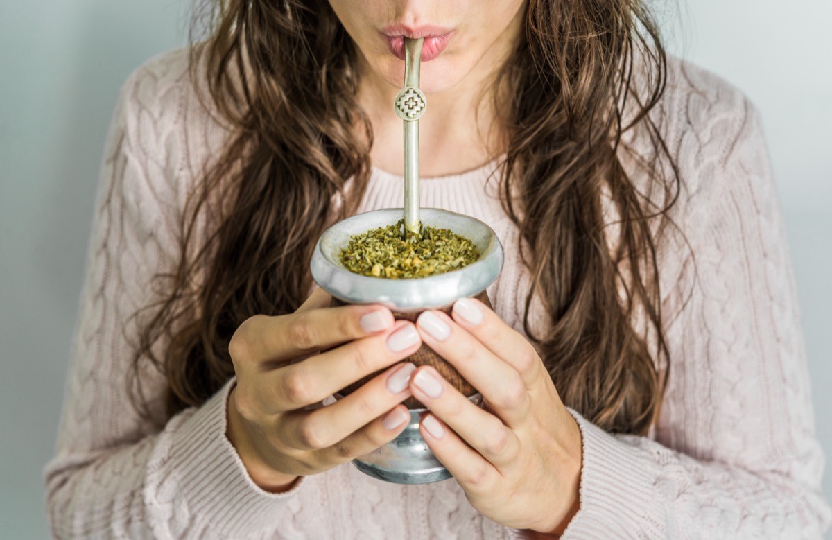 Young woman drinking traditional Argentinian yerba mate tea from a calabash gourd with bombilla stick.