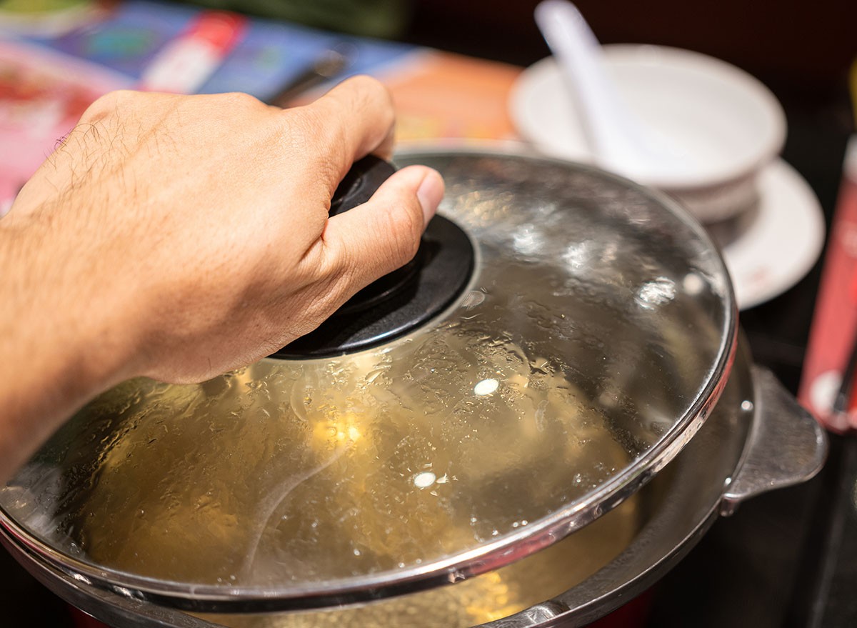 Action of people hand is preparing to open the Sukiyaki or Shabu Shabu pottery's lid after water already boiled. Selective focus photo.