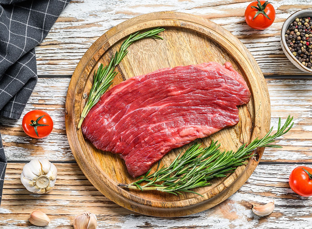 Raw Flank steak on a cutting board. Fresh Marble beef meat black Angus. White wooden background. Top view