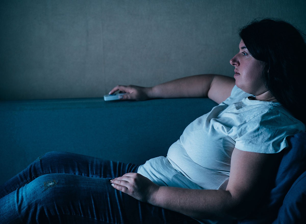 Laziness, sedentariness, overweight, daily routine, television addiction. Woman sitting at coach watching TV late at night