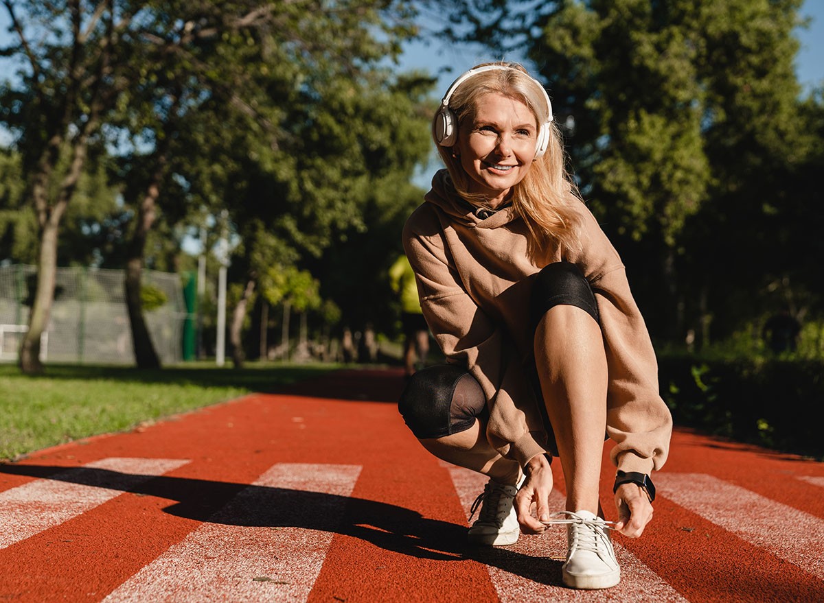 Caucasian mature female runner athlete tying training shoes while jogging on the stadium in public park in the morning. Active healthy sporty lifestyle.