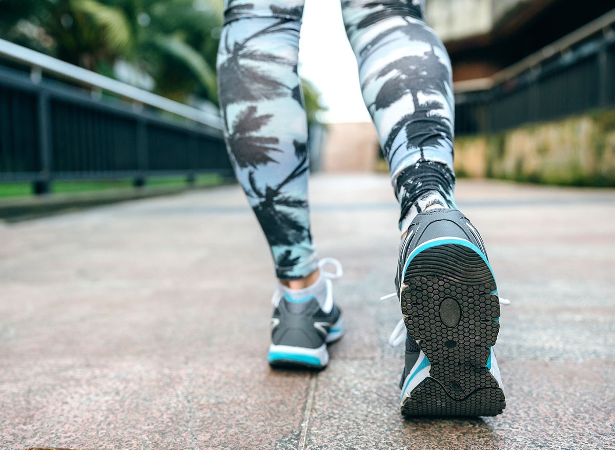 Close up of unrecognizable young woman legs ready to run wearing sneakers and tropical leggings with palm trees