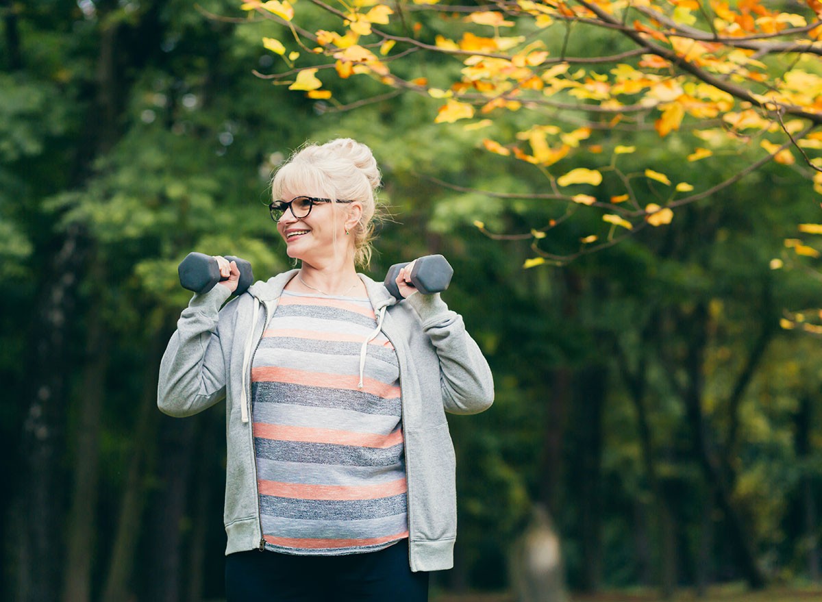 Beautiful senior woman on a walk in the park, performs exercises with dumbbells in her hands