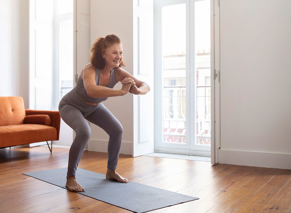Home Workout. Smiling Senior Woman Doing Squats While Training In Living Room, Sporty Elderly Lady Exercising On Fitness Mat, Older Female Making Weight Loss Exercises, Enjoying Active Lifestyle