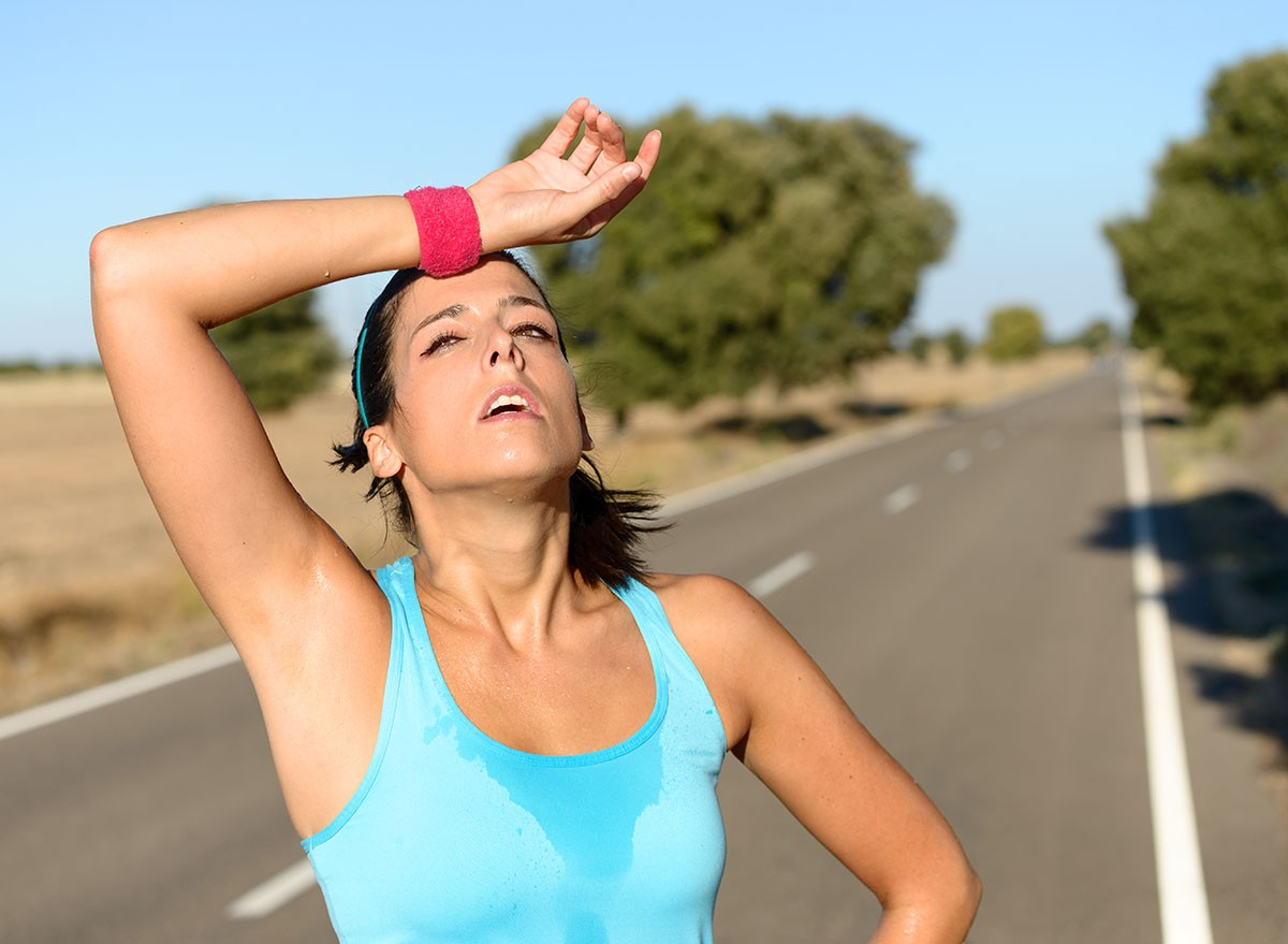 Tired runner sweating after running hard in countryside road. Exhausted sweaty woman after marathon training on hot summer. Hispanic brunette female athlete outdoors.
