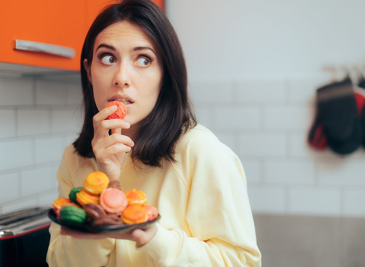 Woman Eating Macarons Feeling Guilty and Hiding. Adult person with sugar addiction hiding her alimentary habits over indulging because of stress. Processed Foods