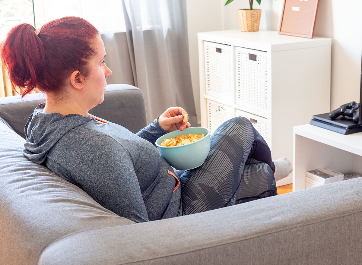 Middle age woman relaxing on the sofa, watching TV and  eating chips