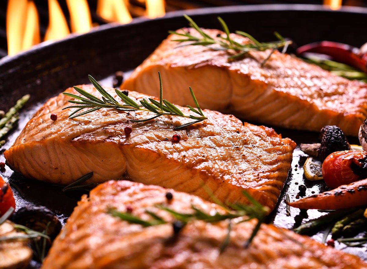 Grilled salmon fish with various vegetables on pan on the flaming grill