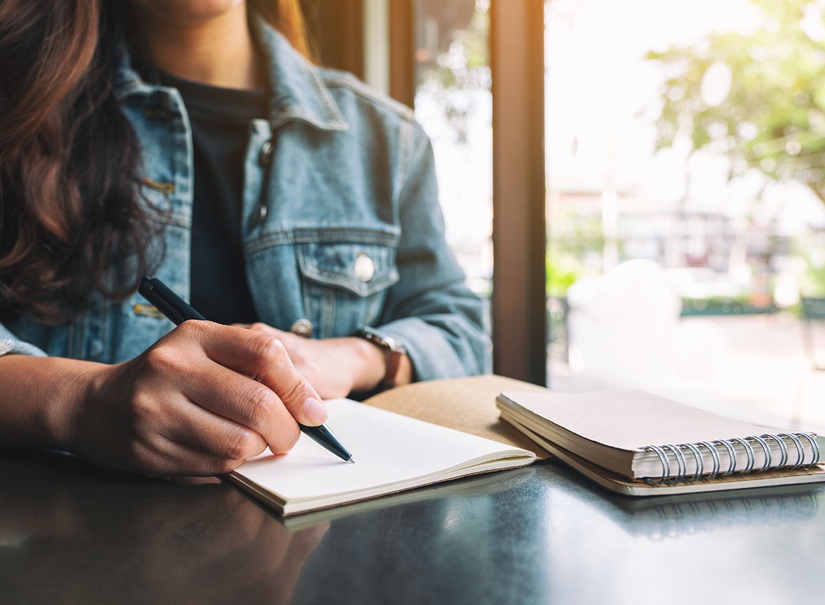 Closeup image of a woman writing on a blank notebook on wooden table