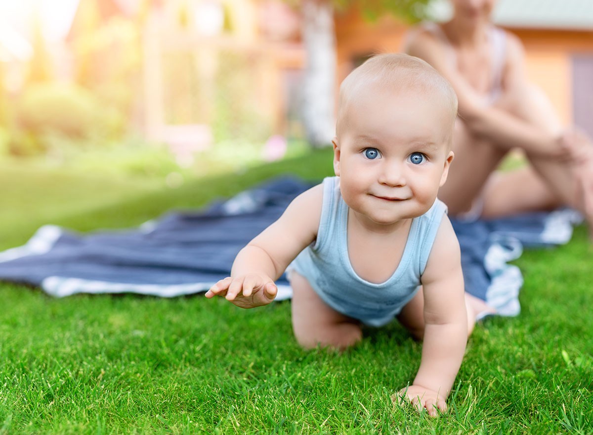 Portrait of cute little caucasian boy having fun in garden with mother. Child crawling on green grass lawn during walk with mom in yard. Happy childhood and baby healthcare.