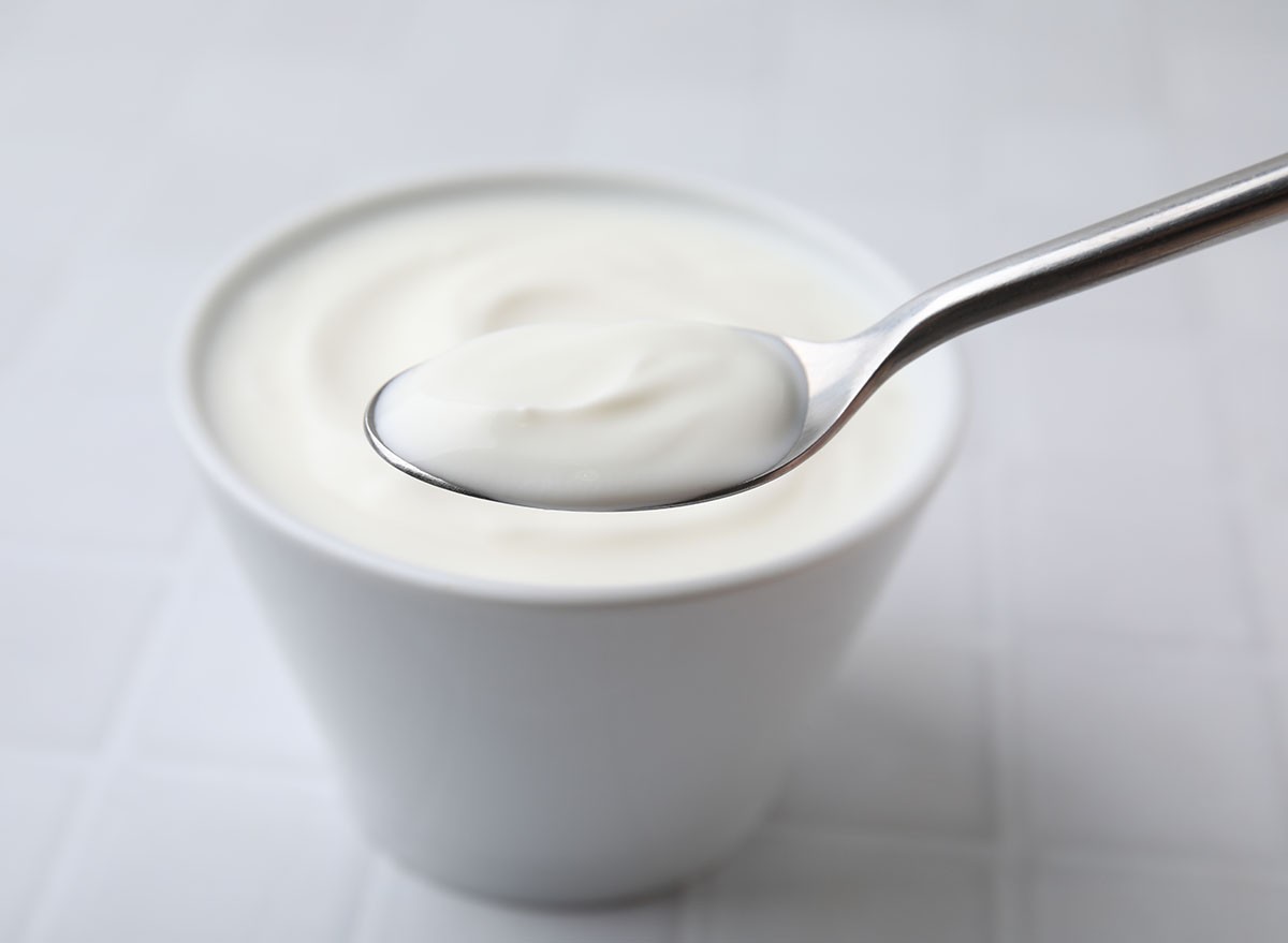 Eating delicious natural yogurt at white tiled table, closeup