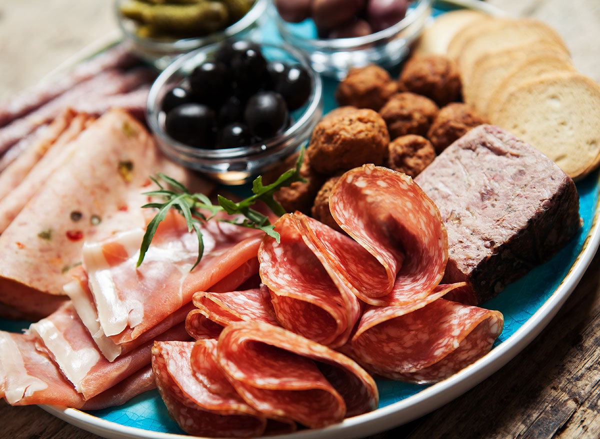 Charcuterie assortment, olives and gherkins on plate on wooden background