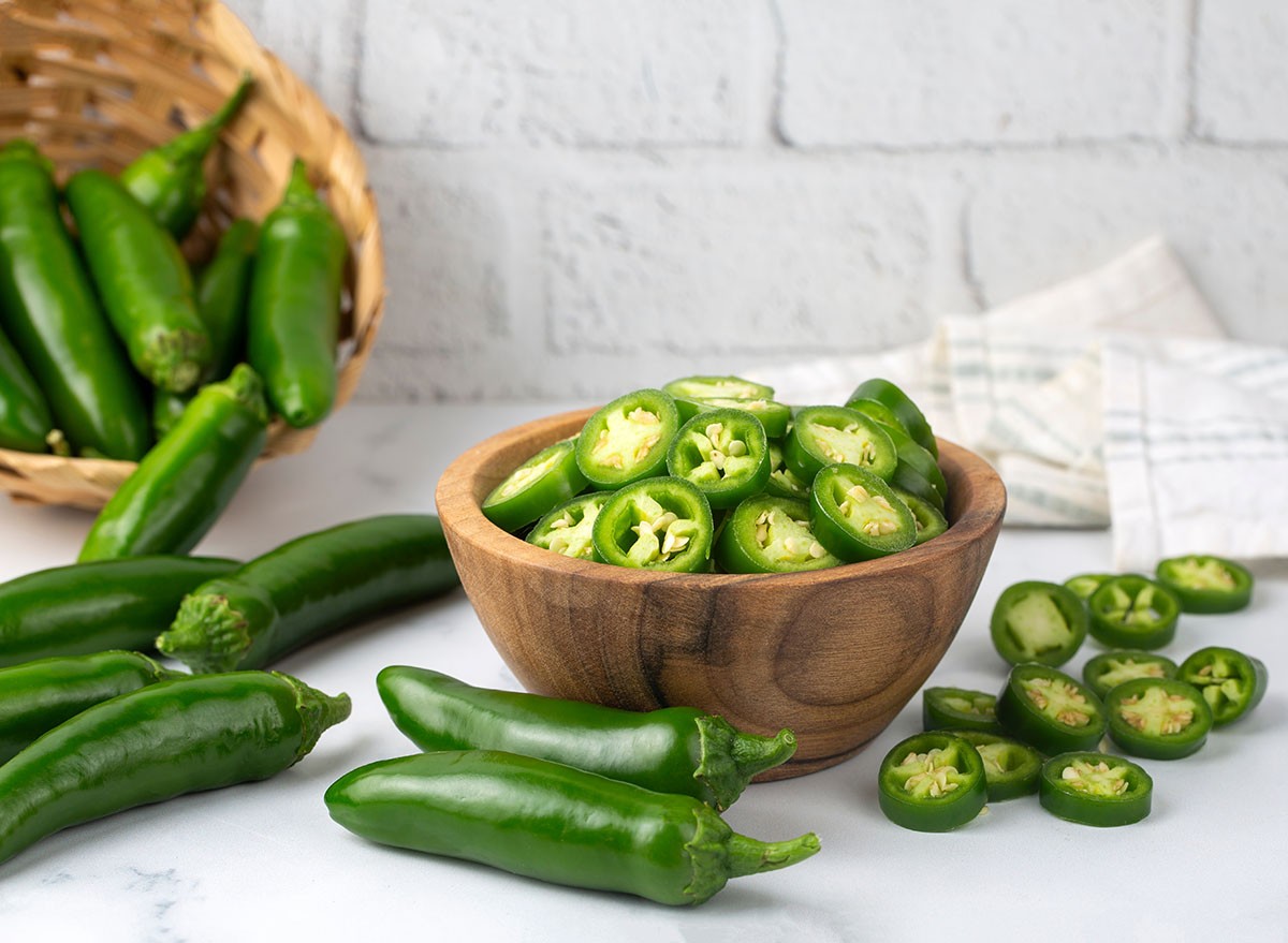 Sliced jalapeno pepper in wooden bowl isolated on white background. Green chili pepper