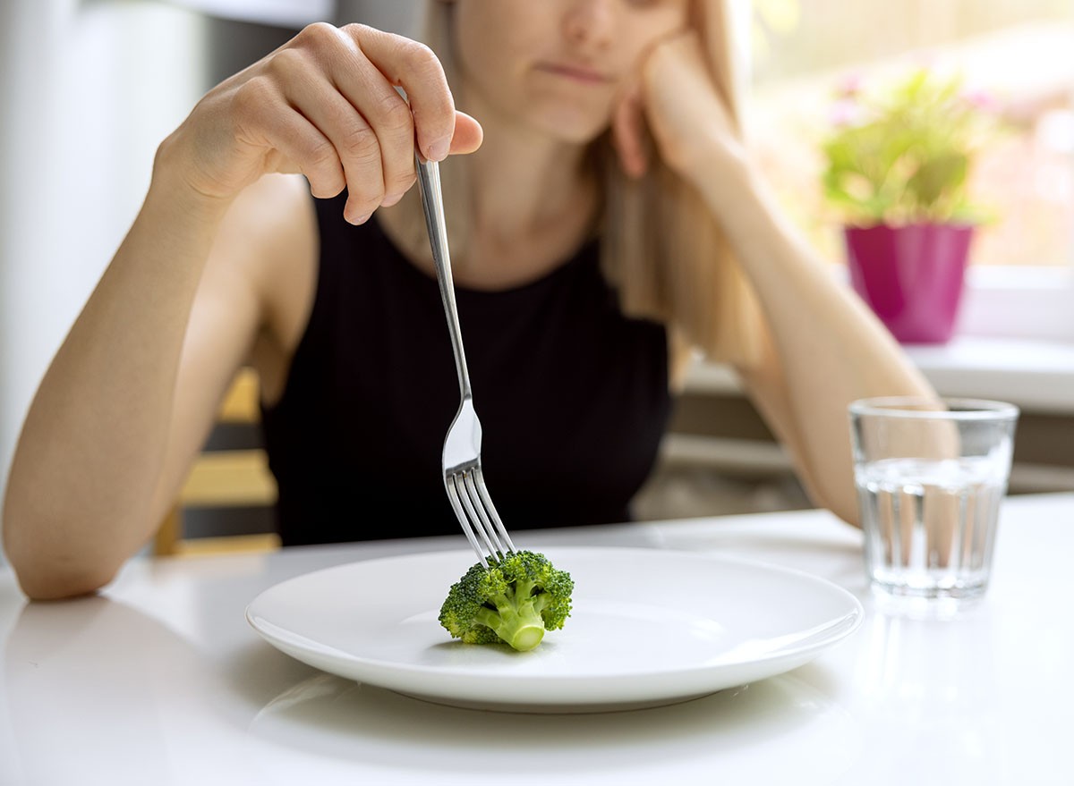dieting problems, eating disorder - unhappy woman looking at small broccoli portion on the plate
