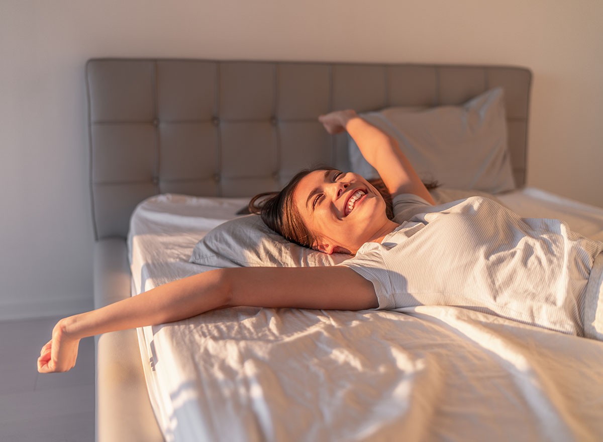 Happy woman lying in comfortable foam latex mattress bed in luxury hotel enjoying relax weekend getaway jumping in bed. Enjoying Asian woman with open arms in freedom.