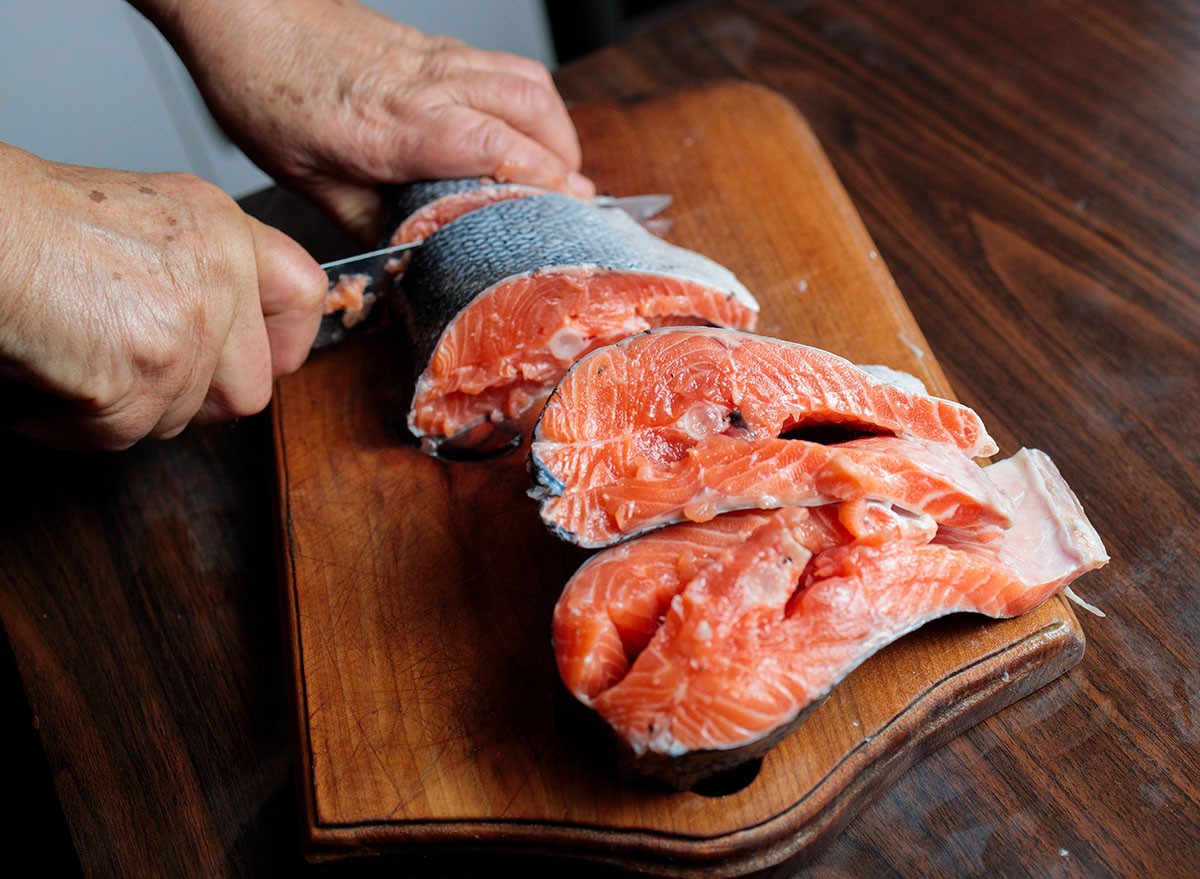 Close up of hands of a Latin person filleting fresh Chilean salmon steak using knife in her kitchen at home