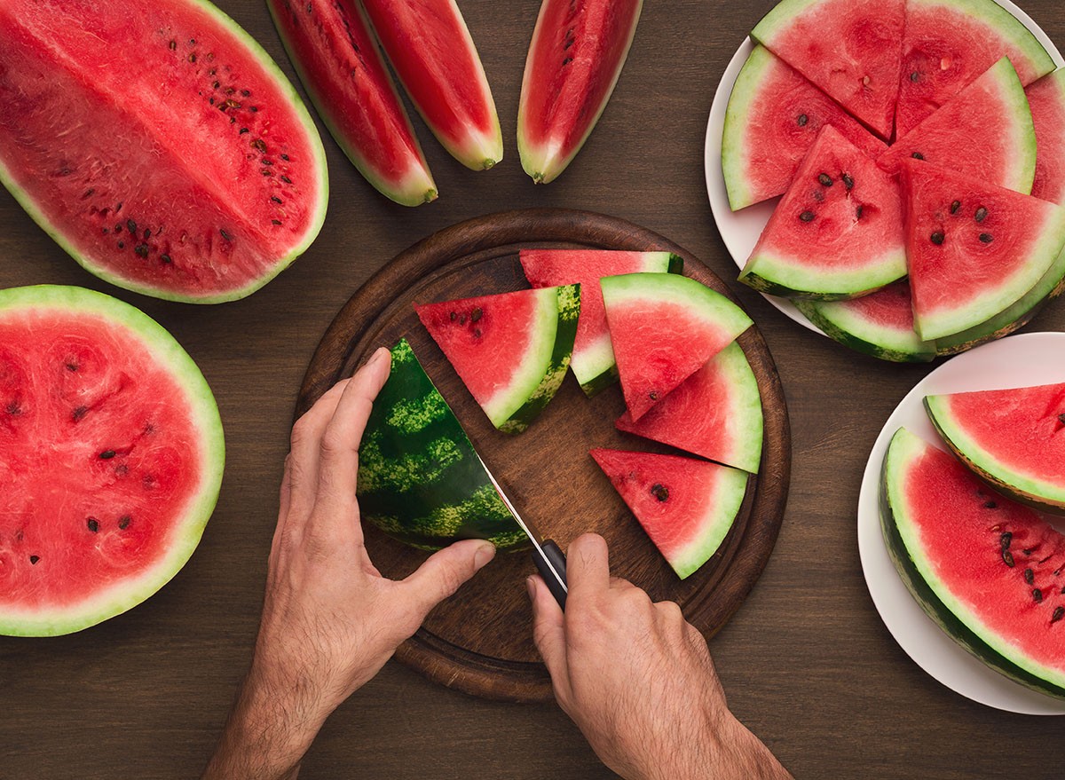 Serving watermelon. Male hands cutting red ripe fruit with knife into slices, kitchen table background, top view