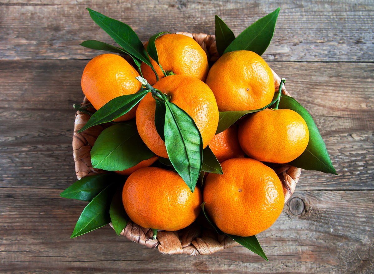 Tangerines (oranges, mandarins, clementines, citrus fruits) with leaves in basket over rustic wooden background, copy space
