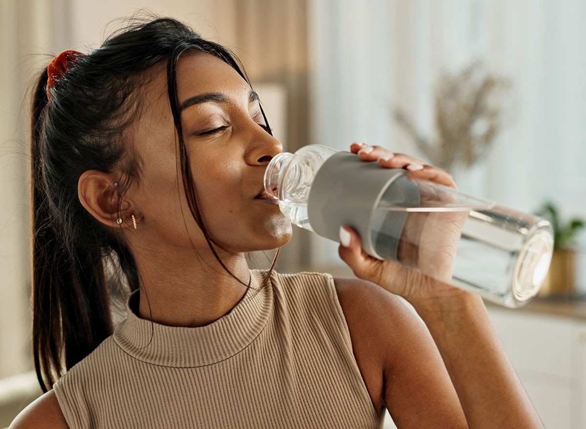 Drinking water, yoga or Indian woman in home with health, fitness or wellness for natural hydration. Thirsty female person, tired or healthy girl with liquid bottle after pilates to detox or relax