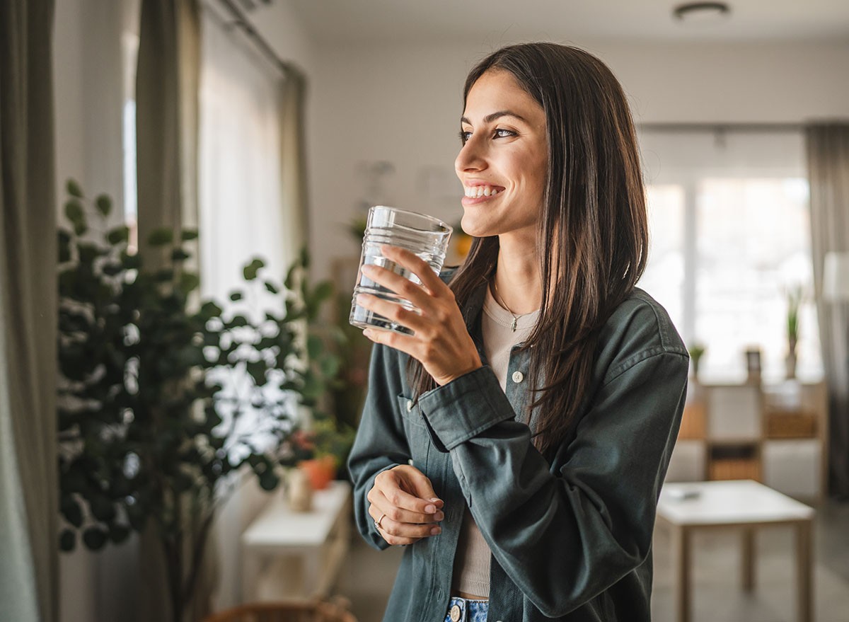 Portrait of adult women stand hold glass of water and look out the window