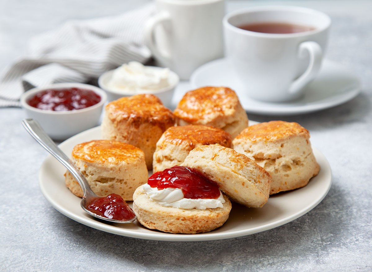 scones on a white plate, a jar of strawberry jam and a cup of tea on a gray background