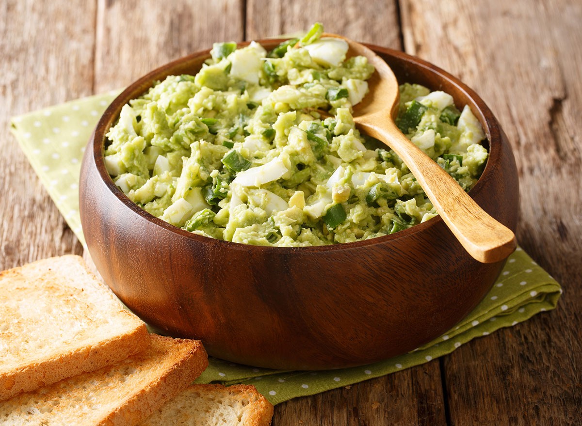 Diet avocado salad with boiled eggs and green onions with yogurt dressing closeup in a bowl on the table. horizontal