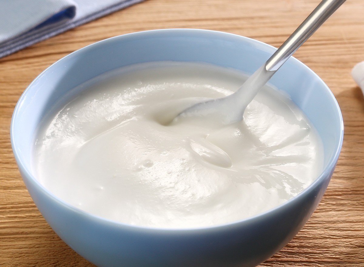 Sour cream is stirred with a spoon in a bowl on a wooden background. Close up. High angle view.