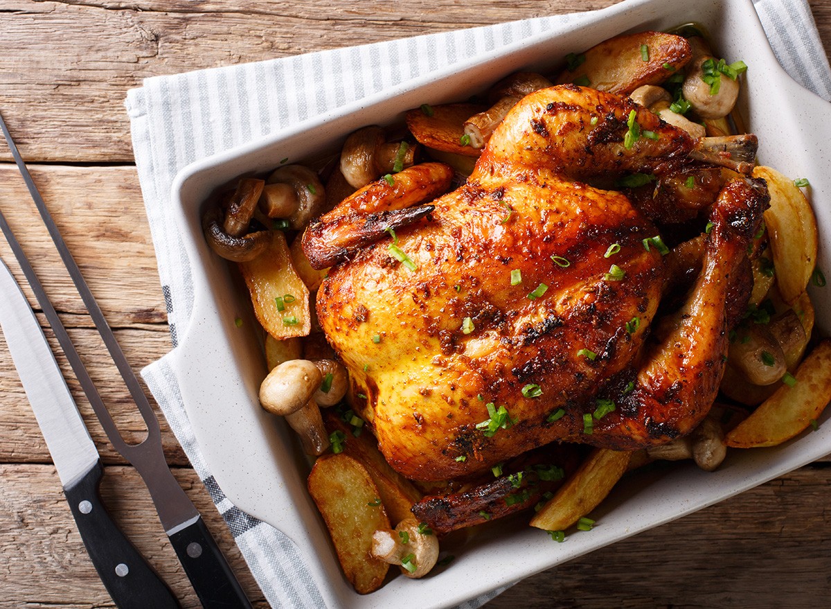 Whole baked chicken with mushrooms and potatoes close-up in a baking dish on a table. horizontal top view from above