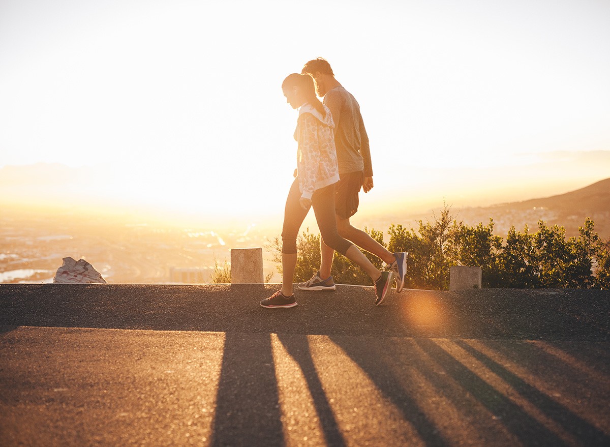 Couple walk along road at sunrise. Couple talking a walk on hillside road with bright sunlight., sun, sunset