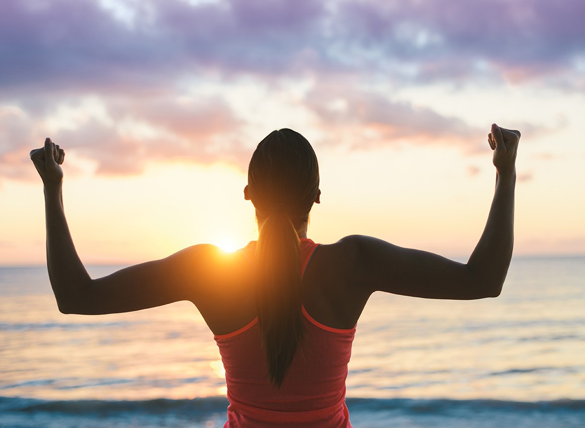 Fitness woman celebrating fitness workout success and motivation towards the sea and sunset.