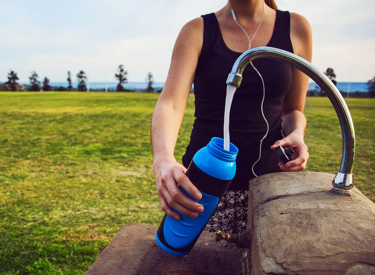Female runner fills up water bottle outdoors at the public park