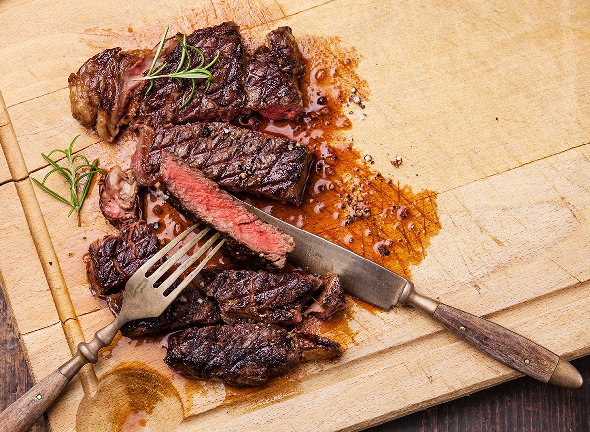 Grilled Ribeye Steak with with knife and fork on meat cutting board on wooden background