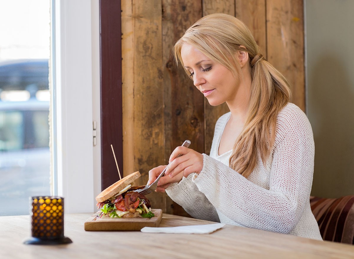 Beautiful young woman eating burger at restaurant